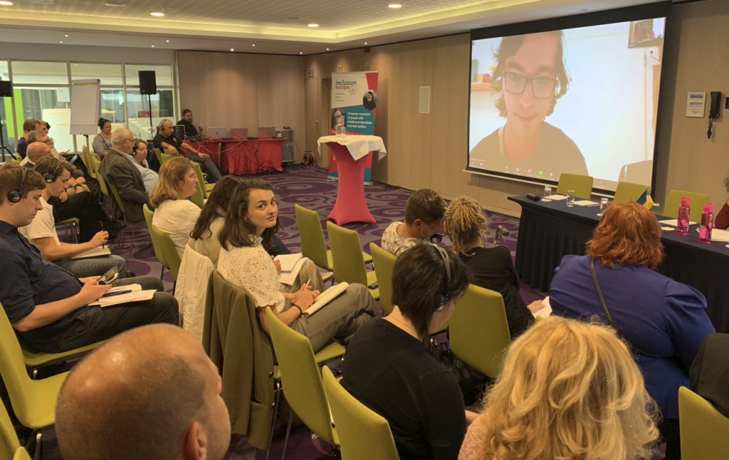 Lukáš Kudlička speaking (on screen) at a conference