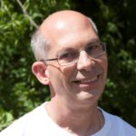 A man with grey hair and glasses smiling into the camera